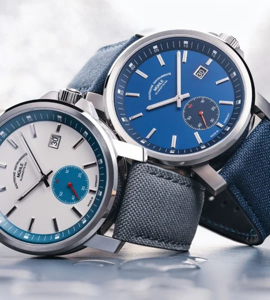 The 29er Big Small Seconds with a stone-white dial and grey strap and the 29er Big Small Seconds with a blue dial and strap are stacked on top of each other on the side.