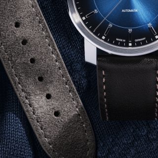 Detailaufnahme der Armbanduhr 29er Casual Küstenblau am braunen Lederband, daneben liegt das graue Velourslederband