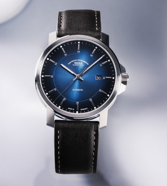 Frontalansicht der Armbanduhr 29er Casual Küstenblau am braunen Lederband auf einem weißen Tisch mit Schattenspiel.