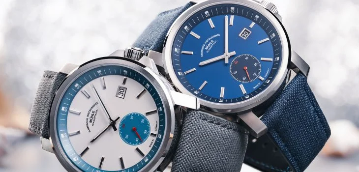 The 29er Big Small Seconds with a stone-white dial and grey strap and the 29er Big Small Seconds with a blue dial and strap are stacked on top of each other on the side.
