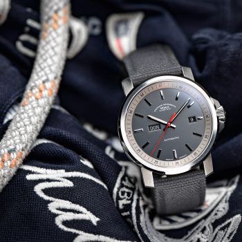 Herrenarmbanduhr 29er Big Tag/Datum mit grauem Zifferblatt am grauen Canvasband steht leicht seitlich auf blau-weißen Stoffen und Seilen.