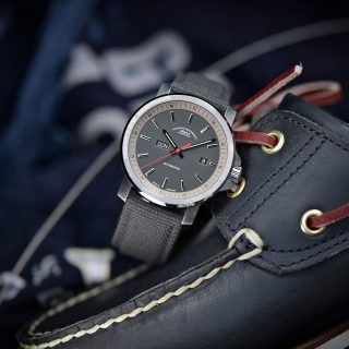 Herren-Automatikuhr 29er Big Tag/Datum mit grauem Zifferblatt am grauen Canvasband steht leicht schräg auf einem dunklen Segelschuh.