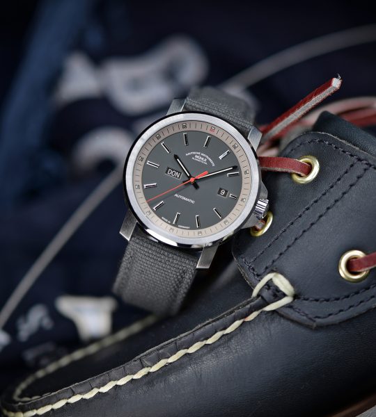 Herren-Automatikuhr 29er Big Tag/Datum mit grauem Zifferblatt am grauen Canvasband steht leicht schräg auf einem dunklen Segelschuh.