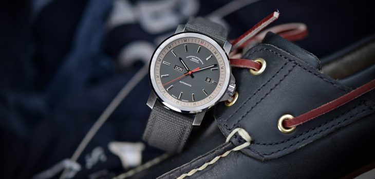 Herren-Automatikuhr 29er Big Tag/Datum mit grauem Zifferblatt am grauen Canvasband steht leicht schräg auf einem dunklen Segelschuh.