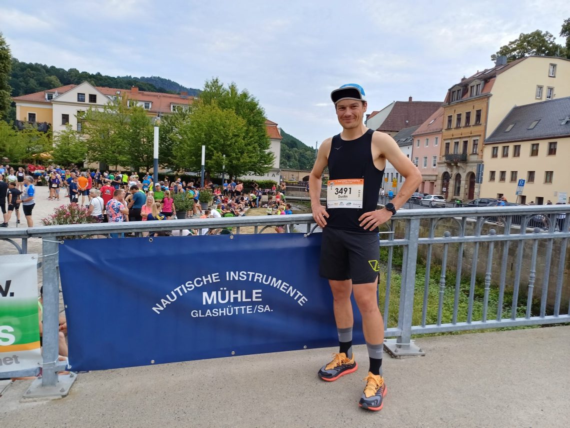 Dustin Mühle steht mit dunklen Sportsachen vor dem blauen Banner mit Mühle-Logo.