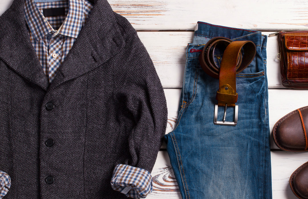 Eine graue Jacke mit innen liegendem karierten Hemd und eine blaue Jeans liegen auf weißen Holzdielen.