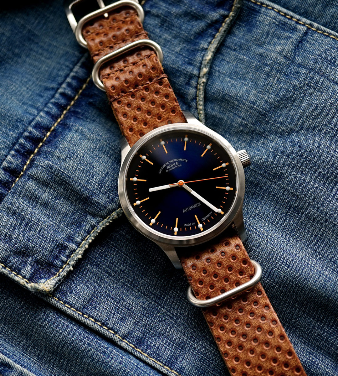Armbanduhr Panova Blau am braun-geprägten Lederband liegt auf einer hellblauen Jeansjacke.
