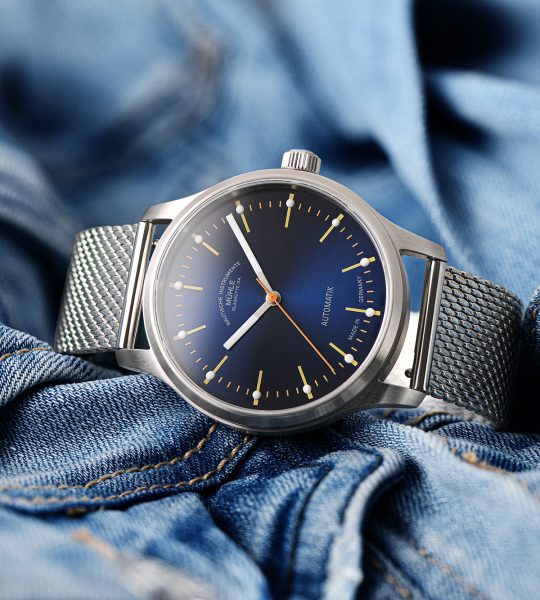 Armbanduhr Panova Blau am Milanaiseband liegt seitlich auf einer hellblauen Jeansjacke.