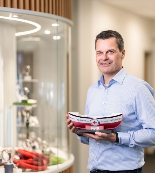 Thilo Mühle vor einer Uhrenvitrine, in der Hand das Sammelschiffchen der DGzRS.
