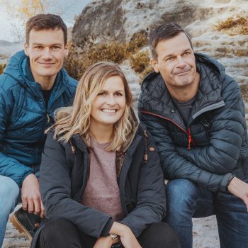 Dustin, Fanny und Thilo Mühle sitzen mit legeren Outdoorjacken bekleidet auf einem Felsen in der Sächsischen Schweiz.