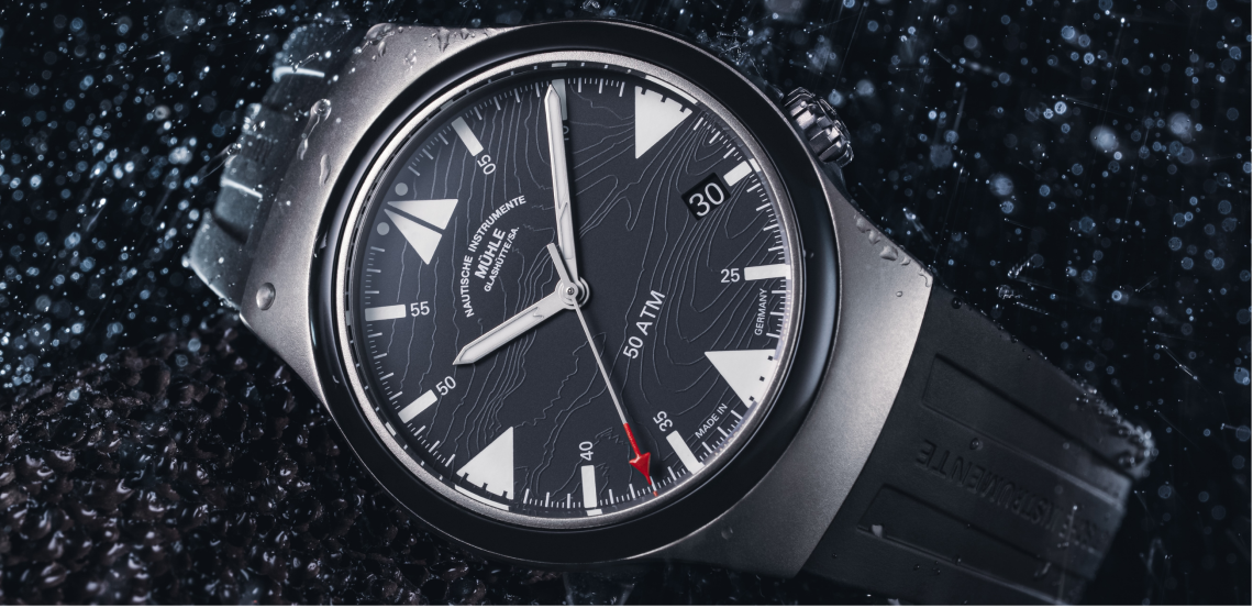 Armbanduhr S.A.R. Mission-Timer "160 Jahre DGzRS" am schwarzen Kautschukband liegt leicht schräg auf einer schwarzen Oberfläche im Regen.