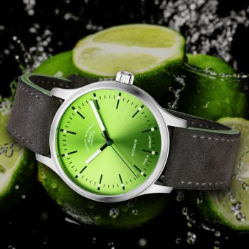 Armbanduhr Panova Limettengrün am grauen Veloursband liegt seitlich vor mehreren Limetten und Wasserspritzern.