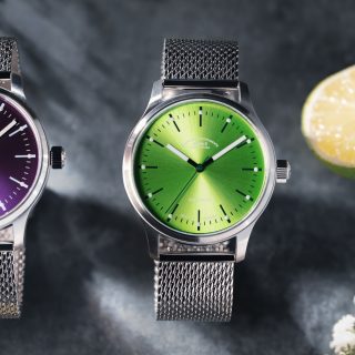 Armbanduhr Panova Limettengrün am Milanaiseband steht auf einer grauen Oberfläche mich Schattenspiel. Daneben die Panova Violett und eine Limette.