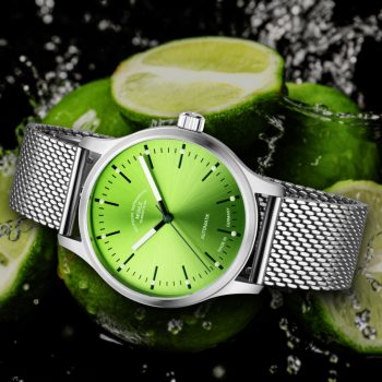 Armbanduhr Panova Limettengrün am Milanaiseband liegt seitlich vor mehreren Limetten und Wasserspritzern.