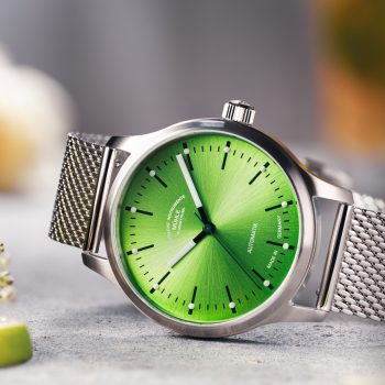 Armbanduhr Panova Limettengrün am Milanaiseband liegt seitlich auf einem hellgrauen Tisch.