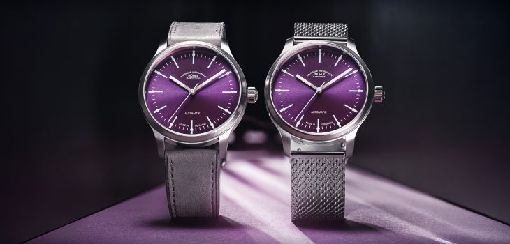 Zwei Armbanduhren (Panova Violett am grauen Lederband und am Milanaiseband) stehen nebeneinander auf einer violetten Oberfläche.