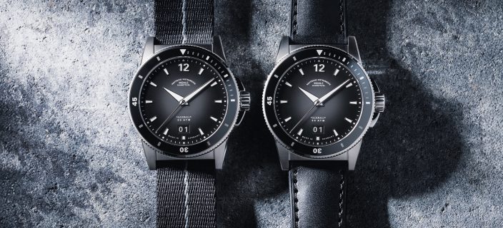 Zwei mechanische Sportuhren Sportivo Großdatum mit schwarzem Zifferblatt, schwarzer Lünette und silbernem Gehäuse am schwarzen Textilband (links) und am schwarzen Leder-/Kautschukband (rechts) liegen auf einer Betonoberfläche.