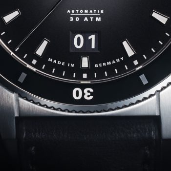 Detailbild der Armbanduhr Sportivo Großdatum mit schwarzem Zifferblatt, schwarzer Lünette und silbernem Gehäuse am schwarzen mit Fokus auf den Gehäuserand bei 6 Uhr.