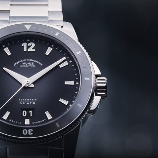 Frontalaufnahme der Armbanduhr Sportivo Großdatum mit schwarzem Zifferblatt, schwarzer Lünette und silbernem Gehäuse am Metallband.