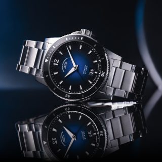 Die sportliche Armbanduhr Sportivo Großdatum mit tiefblauem Zifferblatt am Edelstahlband liegt seitlich auf einer spiegelnden Oberfläche.