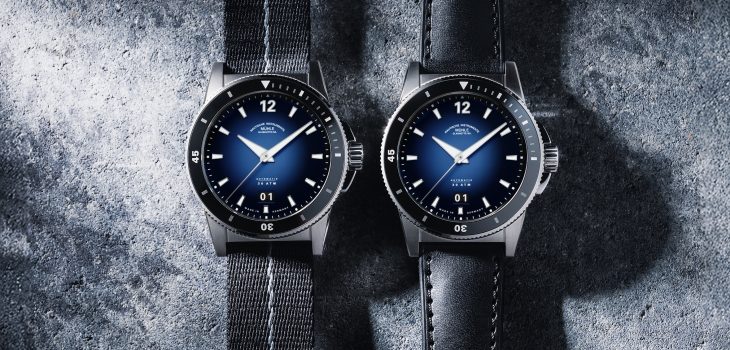 Zwei Modelle der Sportivo Großdatum in Tiefblau liegen nebeneinander vor einem Stein-Hintergrund. Ein Modell mit Textilband, das andere mit Leder-/Kautschukband.