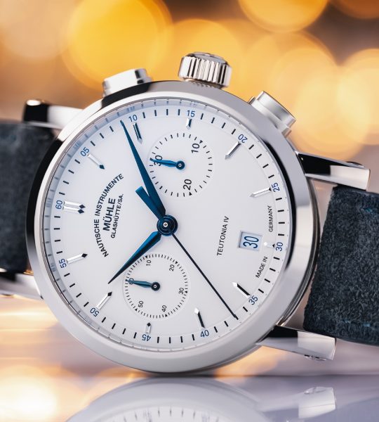 Armbanduhr Teutonia IV Chronograph mit weißem Zifferblatt im weißen Gehäuse am blauen Velourslederband liegt seitlich auf einer weißen Oberfläche mit Lichtpunkten im Hintergrund.