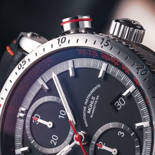 Teutonia Sport I: Nahaufnahme des rot markierten Startdrückers an einer Armbanduhr mit schwarzem Zifferblatt und silbernem Gehäuse.