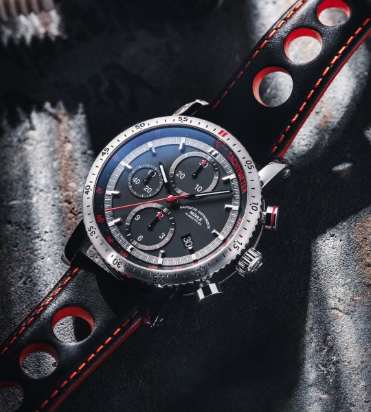 Armbanduhr Teutonia Sport I am schwarzen gelochten Lederband mit roten Highlights liegt auf einem grauen Tisch mit Schattenspiel.