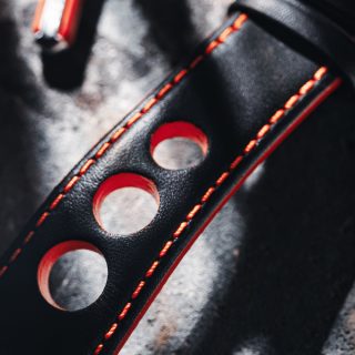 Teil eines schwarzen Lederbandes mit roter Kontrastnaht und drei großen Ausstattungen liegt auf einem Steintisch.